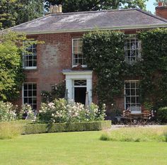 an old brick house with ivy growing on the front and side walls, surrounded by lush green grass