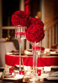 two tall vases filled with red flowers sitting on top of a table covered in silverware