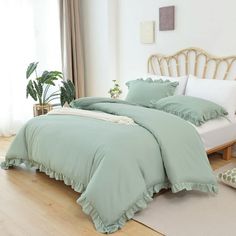 a bed with green sheets and pillows in a white room next to a potted plant