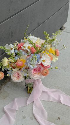 a bouquet of flowers sitting on the ground next to a wall with a pink ribbon