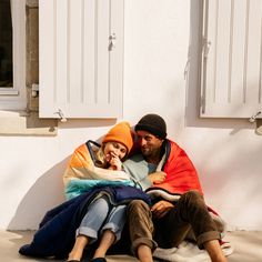 a man and woman sitting on the ground next to each other in front of a building