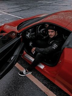 a man sitting in the driver's seat of a red sports car