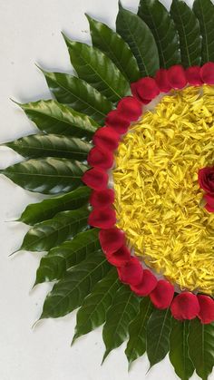 a flower arrangement made out of yellow and red flowers on a white surface with green leaves