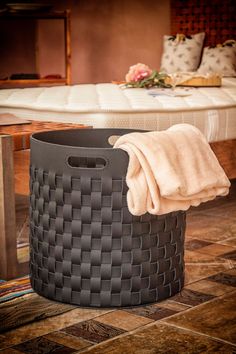 a large basket sitting on top of a tiled floor next to a bed with pillows