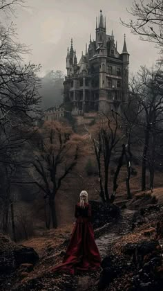 a woman in a long red dress standing on a hill with a castle in the background