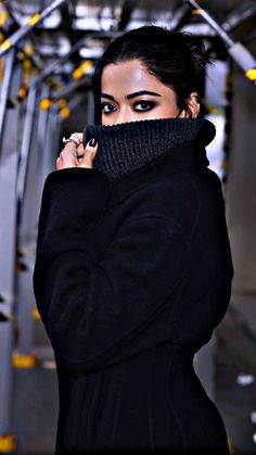 a woman wearing a black coat and scarf with her hands on her face while looking at the camera