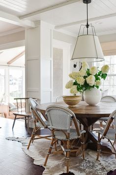 a dining room table with chairs and a vase filled with flowers on top of it