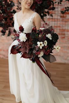 a woman in a white dress holding a bouquet of red and white flowers on her wedding day