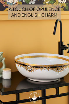 a white bowl with gold trim sitting on top of a black counter next to a faucet