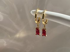 Ruby red dangly hoop earrings Gold plated brass hoop earrings Hoop size approximately 13mm Ruby red cubic zirconia charm size approximately 8mm x 4mm Every item comes in our frosted travel pouch  Gift wrap pouch & box set available, also sold separately Gold And Red Earrings Dangle, Ruby Earrings Aesthetic, Jewelry For Red Dress Formal, Red Dangly Earrings, Red Prom Dress Gold Jewelry, Red Gem Earrings, Gold And Ruby Earrings, Red Dress Accessories Jewelry Formal, Ruby Hoop Earrings