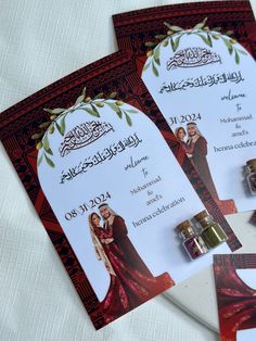 two red and white wedding cards with gold rings on them, sitting next to each other