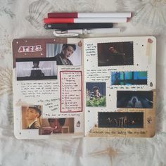 an open notebook with pictures and writing on it, along with two red pens sitting next to each other