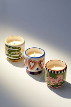 three candles are sitting next to each other on a white surface, one is decorated with an animal and the other has hearts