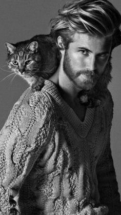 a man with a cat sitting on his shoulders and looking at the camera while wearing a sweater