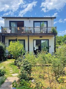 a house that is surrounded by trees and plants on the outside, with a wooden walkway leading to it