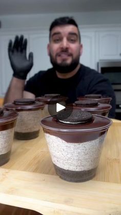 a man sitting at a table with several cups on it and one is holding his hand up to the camera