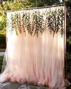 an outdoor wedding ceremony with pink tulle and greenery draped over the altar area