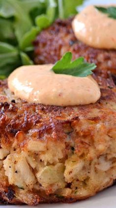 two crab cakes on a white plate with some greens and sauce in the middle, ready to be eaten