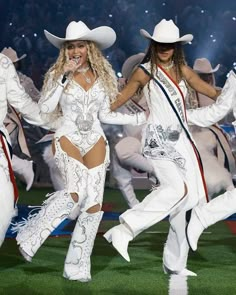 two women in white outfits and cowboy hats are dancing on the field at a football game