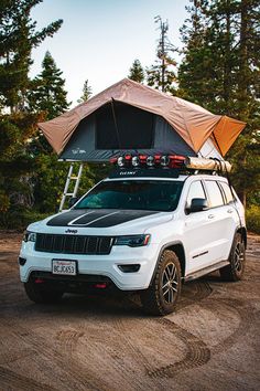 a jeep with a tent attached to the roof is parked in front of some trees