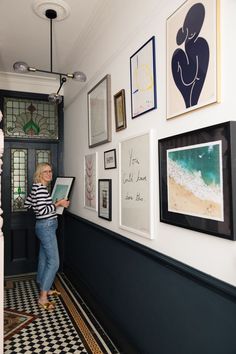 a woman standing in front of a wall with pictures on it and holding a clipboard