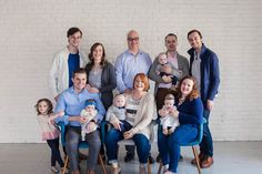 a group of people posing for a photo with their babies and toddlers in front of a white brick wall