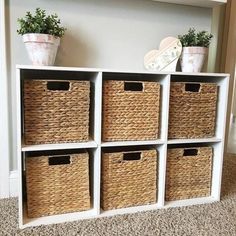 four white shelves with wicker baskets and plants in them on top of carpeted floor