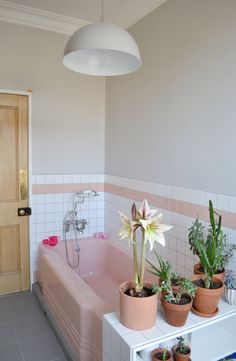 a pink bath tub sitting next to a white sink under a light hanging above it