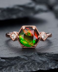 an opal and diamond ring sitting on top of a black rock with two diamonds