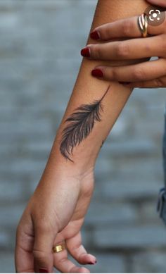 a woman's arm with a small feather tattoo on the left wrist and another hand