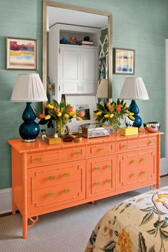 an orange dresser with blue vases and flowers on it in front of a mirror