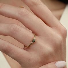 a woman's hand wearing a gold ring with green stones on the middle finger