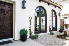 a white house with two large brown doors and plants in front of the entrance door