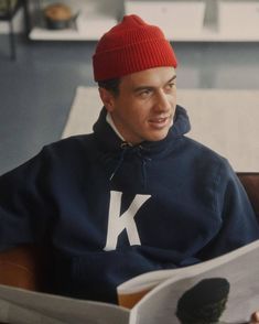 a man in a red hat is reading a paper while sitting on a brown chair