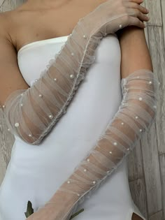 a woman in a white dress wearing long gloves with pearls on the arms and arm