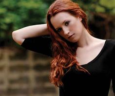 a woman with red hair is posing for the camera and has her hand on her head