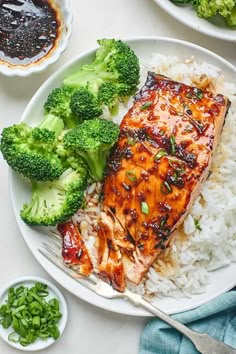 a plate with broccoli, rice and salmon on it next to some sauce