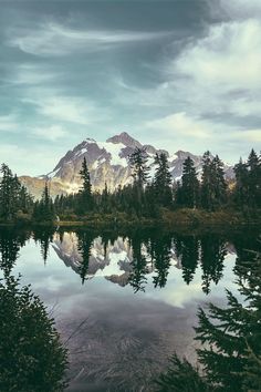 a lake surrounded by trees and mountains under a cloudy sky