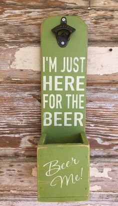 a green beer bottle opener hanging on the side of a wooden wall that says, i'm just here for the beer