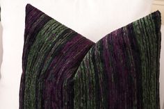 a purple and green striped pillow sitting on top of a white pillow case next to a wall