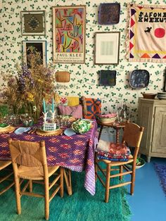 a room with several pictures on the wall and table in front of two wooden chairs