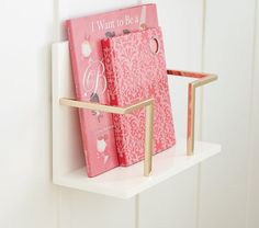 two pink books are sitting on a white shelf