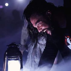 a man with long hair holding a lantern in his hand and looking down at it