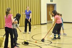 four girls in a gym with brooms and mop