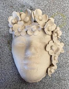 a clay head with flowers on it is laying on the ground in front of a wall