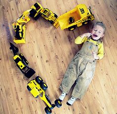 a young boy laying on the floor next to construction equipment and toy cars, with his mouth open