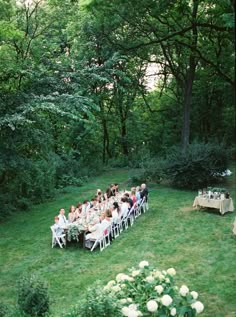 a group of people sitting around a table in the middle of a field next to trees