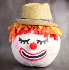 a white pumpkin with a clown face painted on it's side and a straw hat on top