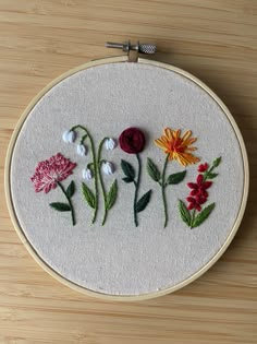 a close up of a embroidery on a wooden surface with flowers in the center and leaves around it