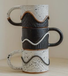 three black and white coffee mugs stacked on top of each other with wavy designs